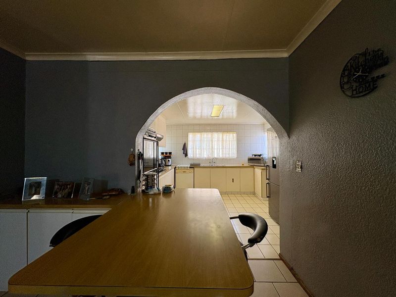 A dated kitchen featuring traditional cabinetry, tiled flooring, and a distinctive arched entryway connecting to the adjacent living space.