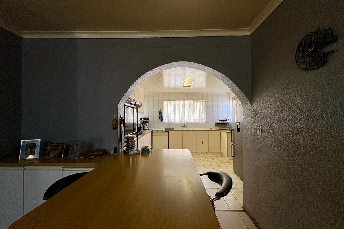 A dated kitchen featuring traditional cabinetry, tiled flooring, and a distinctive arched entryway connecting to the adjacent living space.