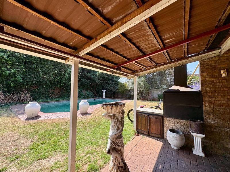 Covered patio area featuring a built-in braai, brick paving, and direct access to the swimming pool and garden.