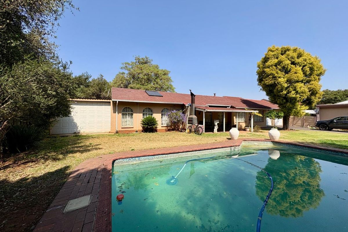 Rear exterior view of the house featuring a swimming pool, covered patio area, and established garden surroundings.