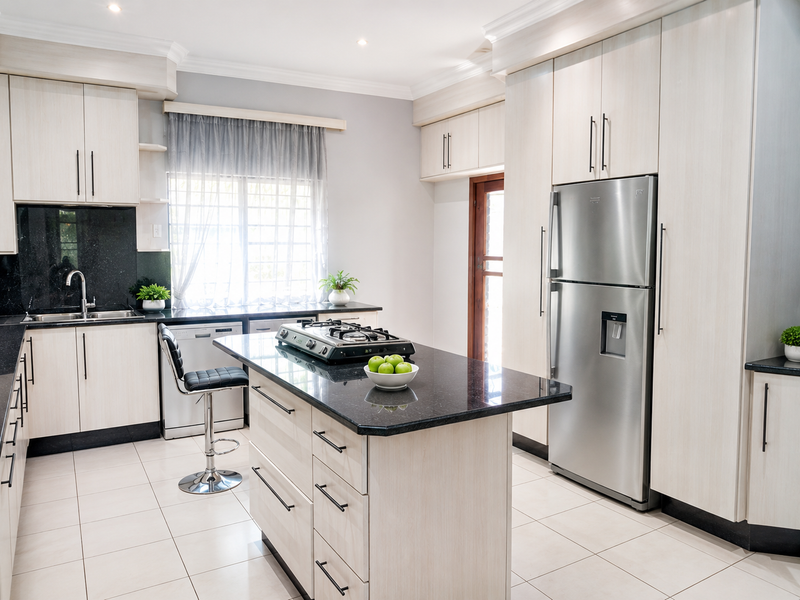 Modern kitchen featuring light wood cabinetry, granite countertops, a central island with a gas hob, and tiled flooring.