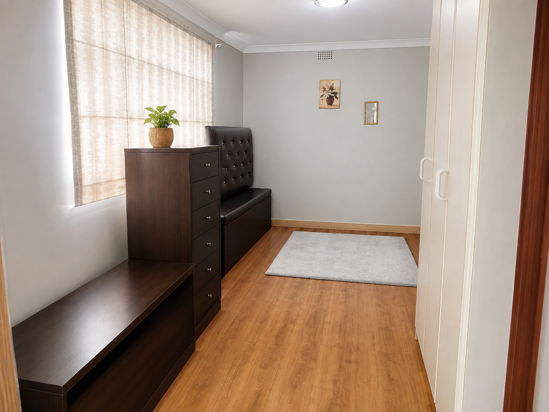 A well-maintained bedroom featuring laminate flooring, built-in wardrobe storage, and neutral wall finishes with roman blinds.