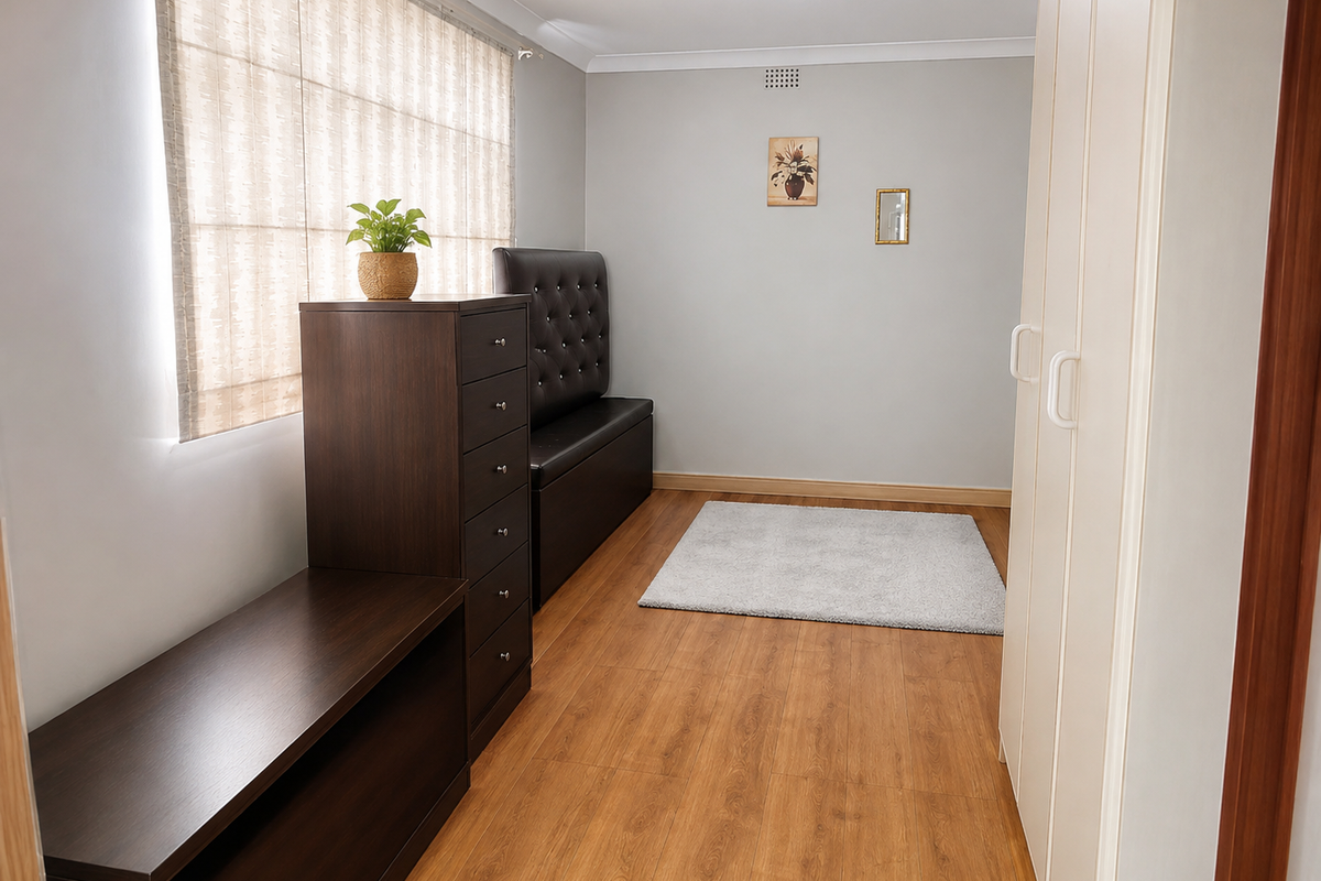 A well-maintained bedroom featuring laminate flooring, built-in wardrobe storage, and neutral wall finishes with roman blinds.