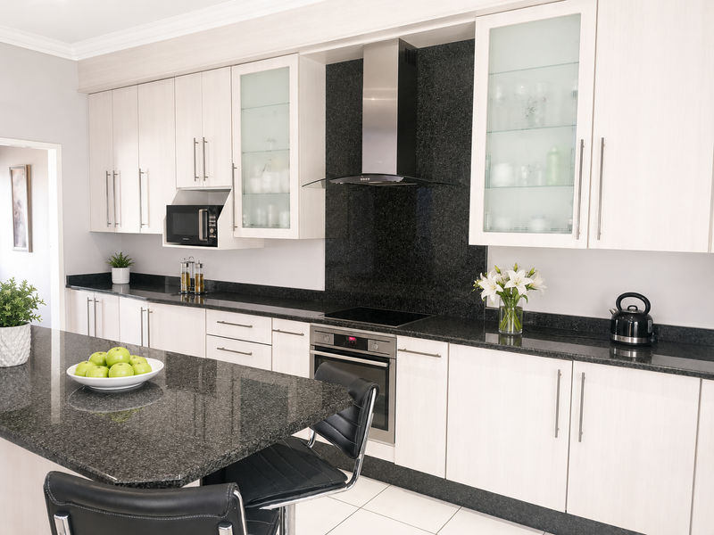 Modern kitchen featuring light wood cabinetry, contrasting black granite countertops, built-in stainless steel appliances, and a central island with breakfast bar seating.