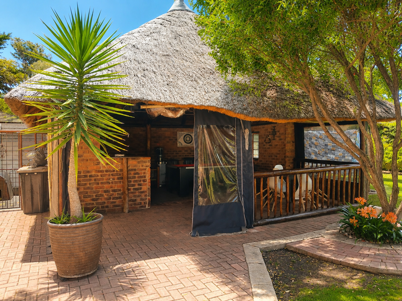 A rustic outdoor entertainment area featuring a thatched roof, brick construction, and a built-in bar, set on a paved patio.
