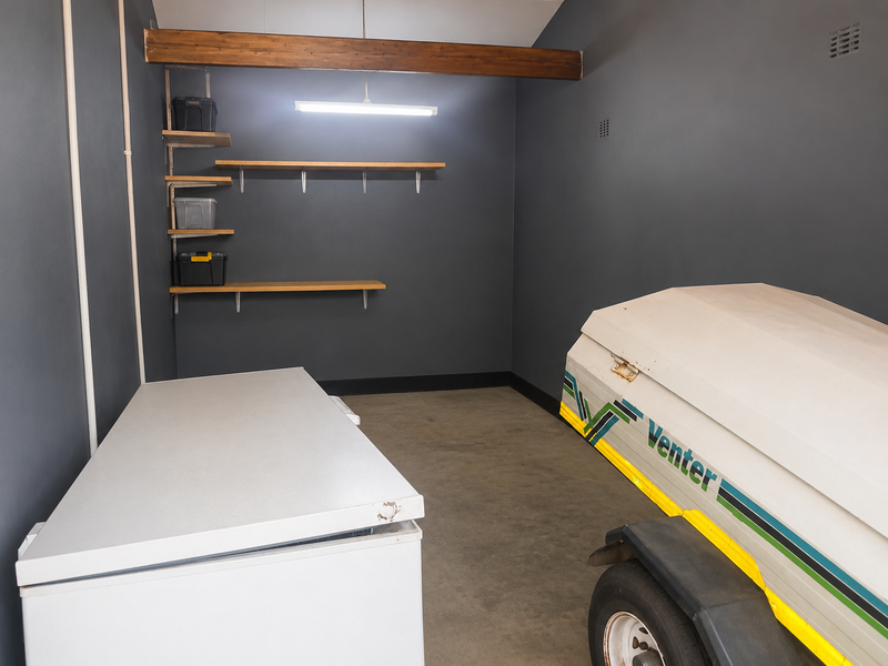 A functional garage space featuring dark painted walls, exposed timber beam detail, concrete flooring, and practical wall-mounted shelving units.