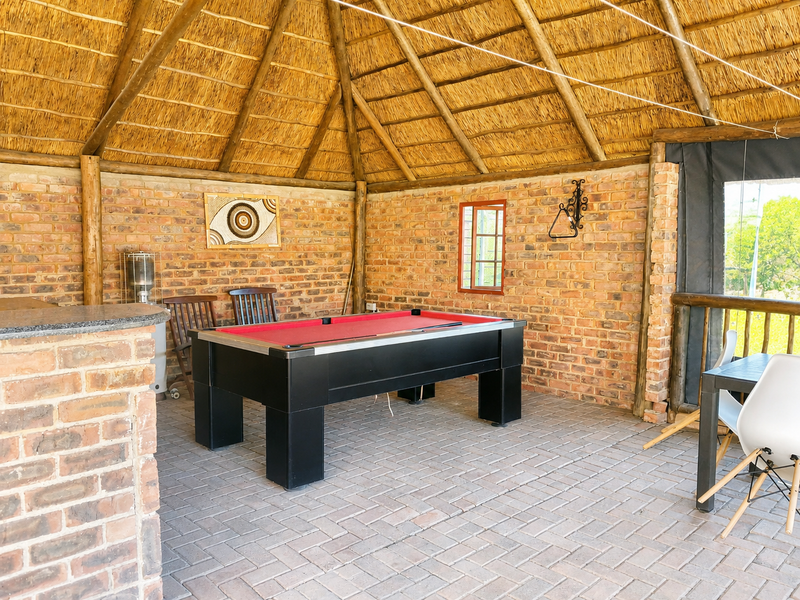 Covered outdoor entertainment area featuring a rustic thatched roof, exposed brick walls, and a built-in brick bar counter, perfect for social gatherings.