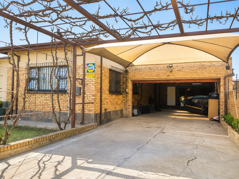 Front exterior view featuring a face brick facade, a concrete driveway, and a covered parking area with a shade sail and metal pergola structure.