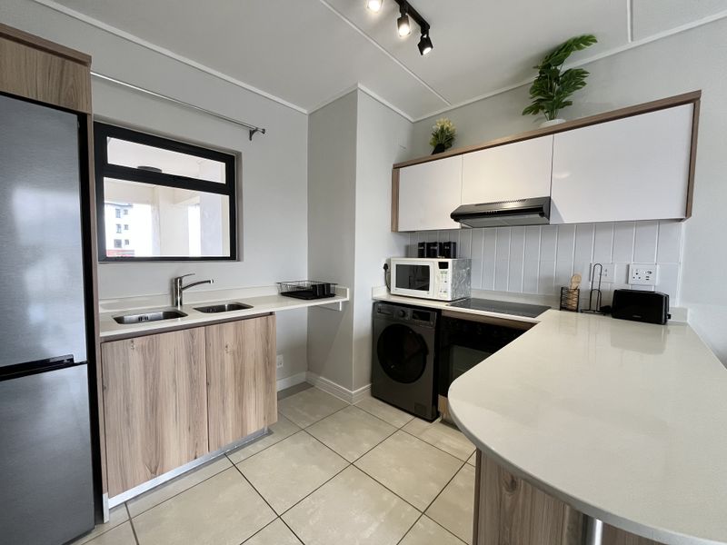 Modern kitchen featuring sleek wood-grain cabinetry, quartz countertops, integrated appliances, subway tile backsplash, and contemporary track lighting.