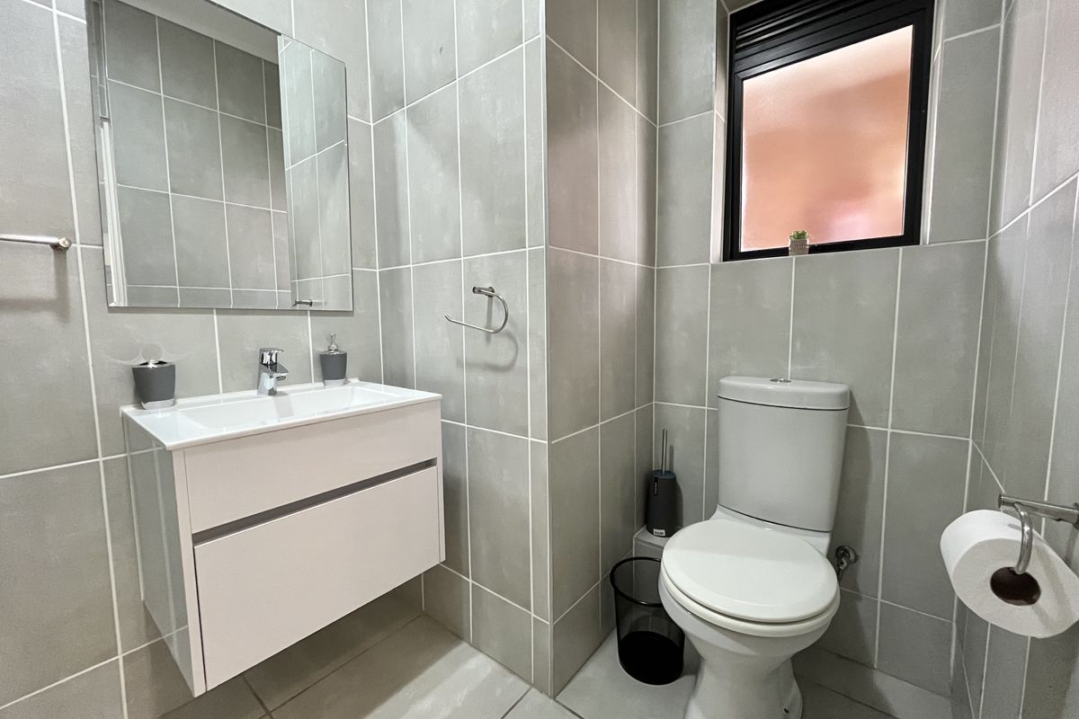 Modern bathroom featuring a wall-mounted vanity, ceramic basin, and full-height wall tiling with a window providing natural light.