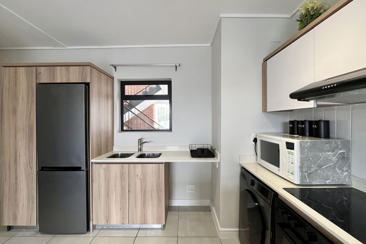 Modern kitchen featuring light wood-grain cabinetry, sleek dark appliances, a double sink, and tiled flooring with a clean, contemporary finish.