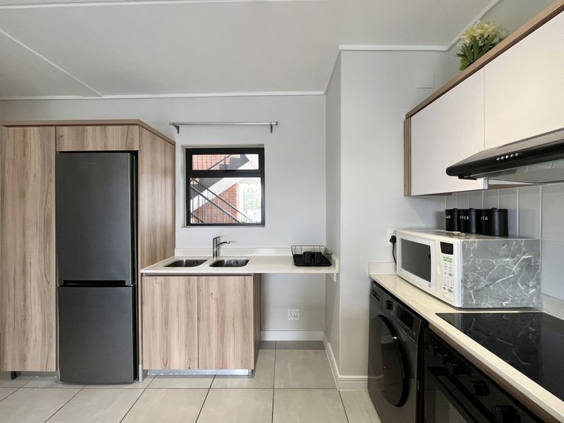 Modern kitchen featuring light wood-grain cabinetry, sleek dark appliances, a double sink, and tiled flooring with a clean, contemporary finish.