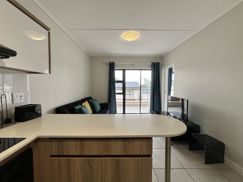 Open-plan living area featuring a modern kitchen with stone countertops, breakfast bar, and direct access to a balcony through sliding glass doors.