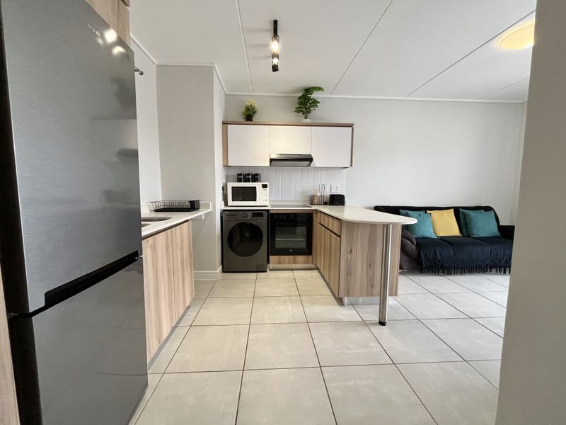 Modern open-plan kitchen featuring light wood cabinetry, integrated appliances, tiled flooring, and a functional breakfast bar layout.