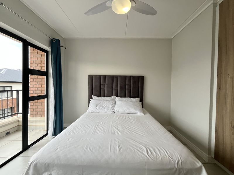 A well-maintained bedroom featuring a ceiling fan, built-in wardrobe, and a sliding glass door providing access to a private balcony.
