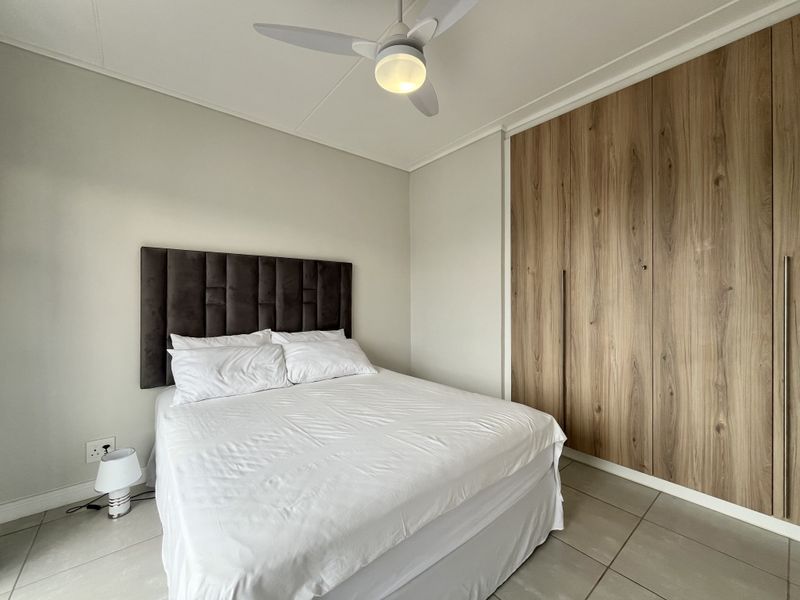 A well-maintained bedroom featuring modern wood-finish built-in cupboards, a ceiling fan, and neutral tiled flooring.