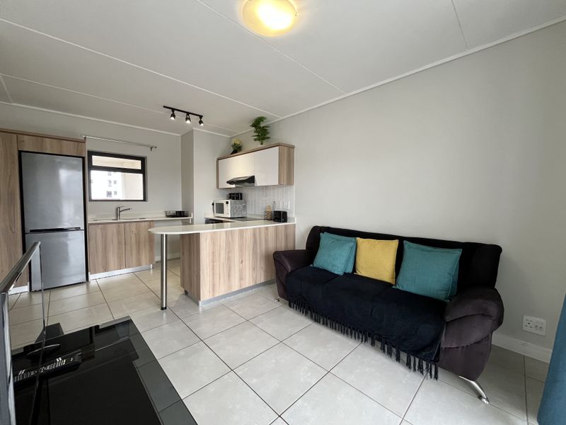 An open-plan living area featuring a modern kitchen with wood-finish cabinetry, a breakfast bar, and tiled flooring throughout.