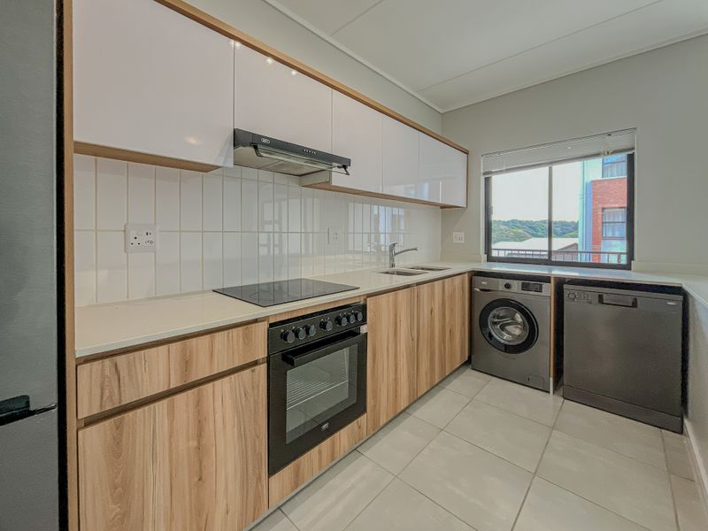 Modern kitchen featuring wood-grain and white cabinetry, electric hob, built-in oven, extractor fan, tiled backsplash, and integrated space for laundry and dishwasher appliances.