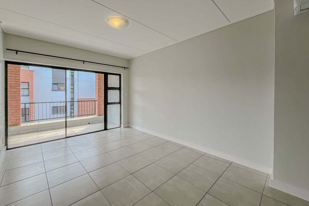A bright, empty living room featuring neutral tiled flooring, a wall-mounted air conditioning unit, and a large sliding glass door leading to a balcony.