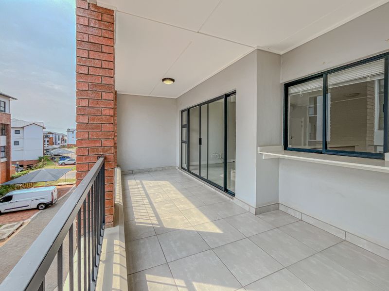 A spacious covered balcony featuring tiled flooring, a metal balustrade, and sliding glass doors providing access to the interior living area.
