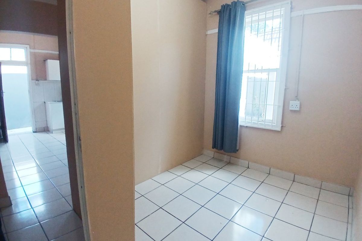 An empty bedroom featuring tiled flooring and a window with security bars, offering a blank canvas for potential interior design updates.