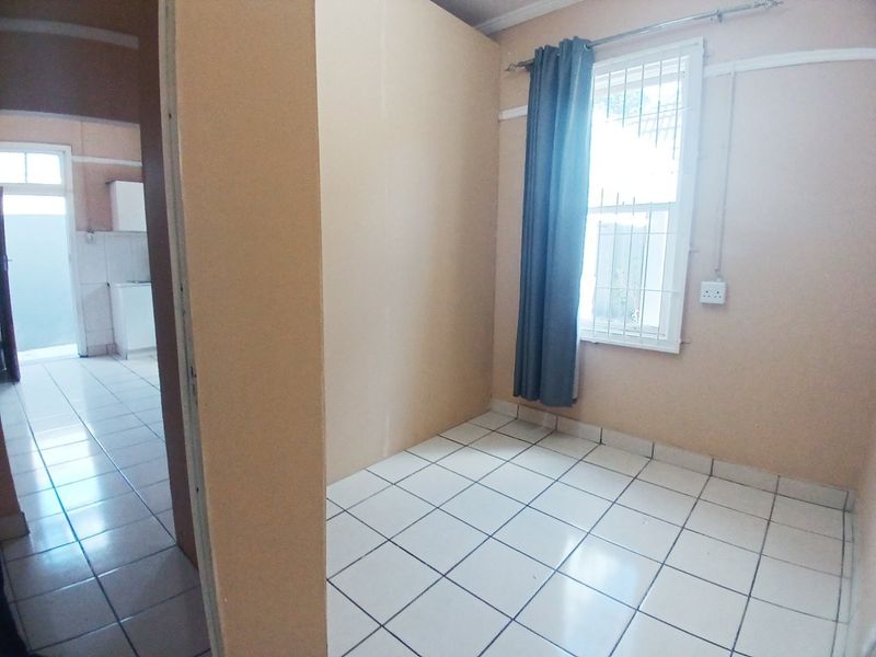 An empty bedroom featuring tiled flooring and a window with security bars, offering a blank canvas for potential interior design updates.