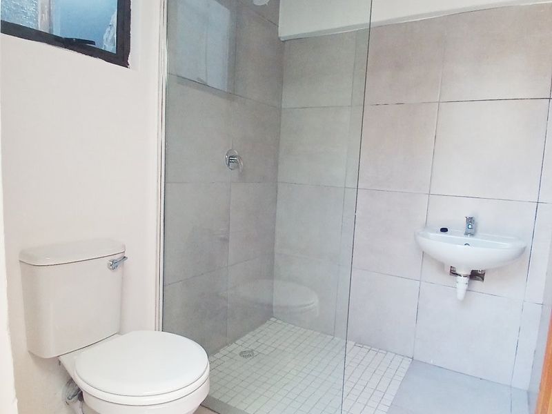 A compact bathroom featuring a glass-enclosed shower, wall-mounted basin, and toilet, with neutral tiling throughout.