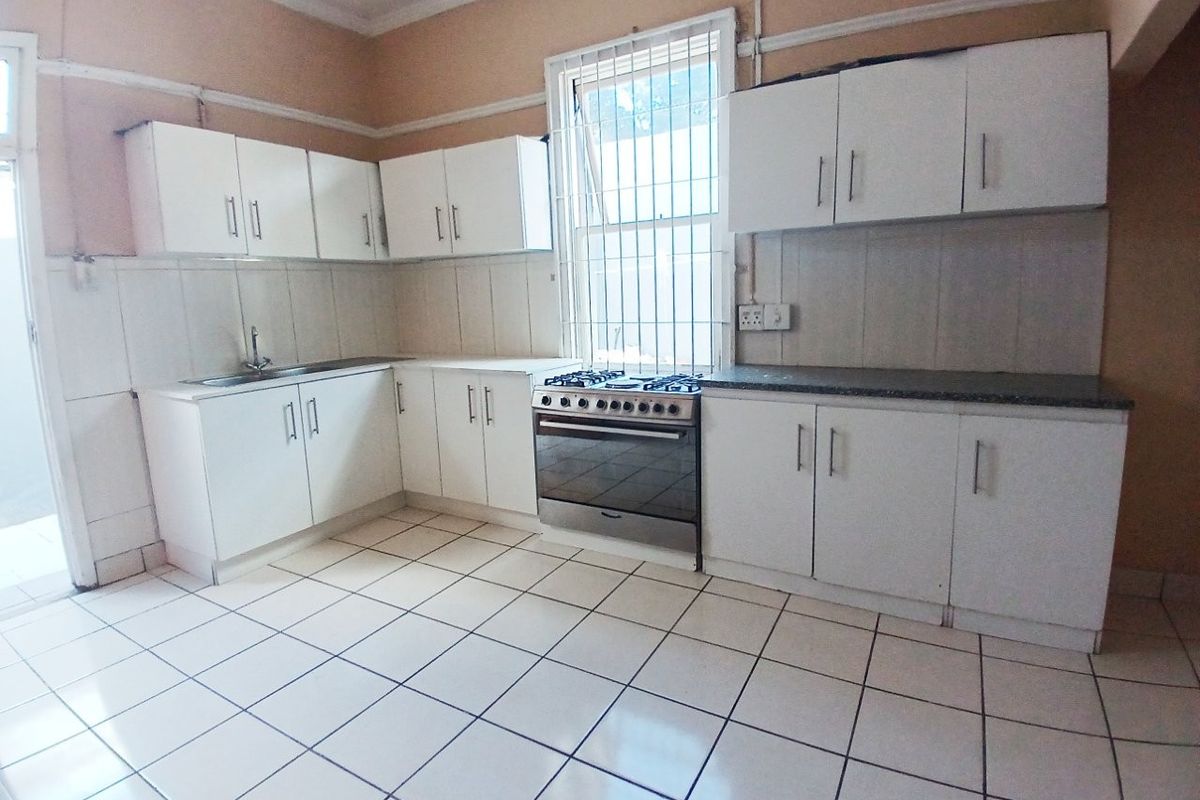A functional kitchen featuring white built-in cabinetry, a stainless steel stove, tiled flooring, and a tiled backsplash with a window providing natural light.