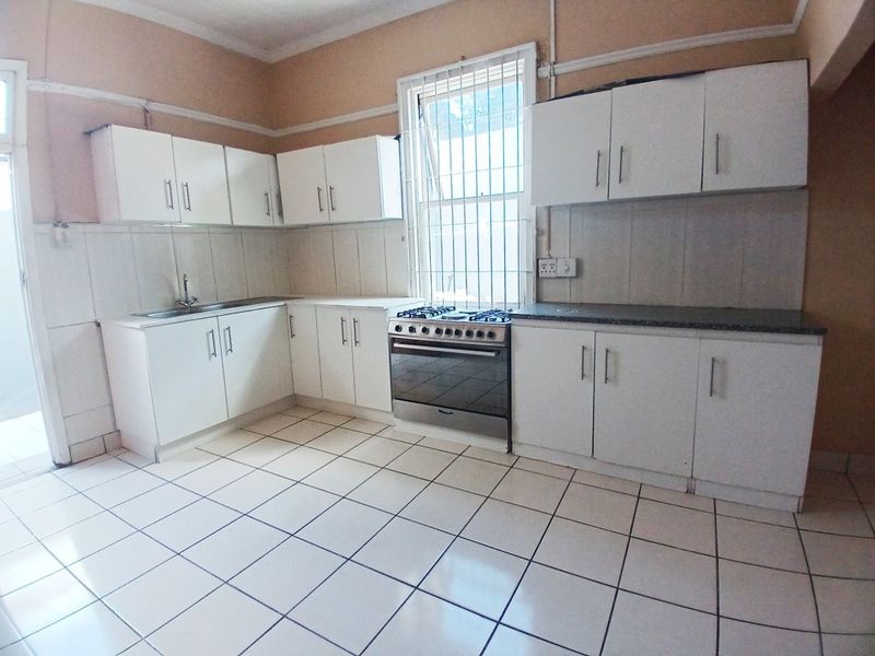 A functional kitchen featuring white built-in cabinetry, a stainless steel stove, tiled flooring, and a tiled backsplash with a window providing natural light.