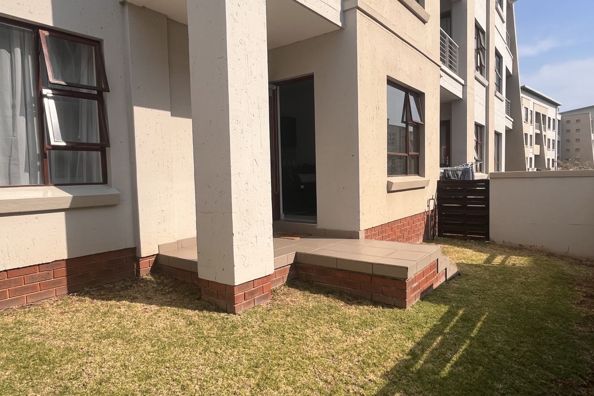 Ground floor apartment exterior featuring a tiled patio area, brick base detailing, and a private lawn space.