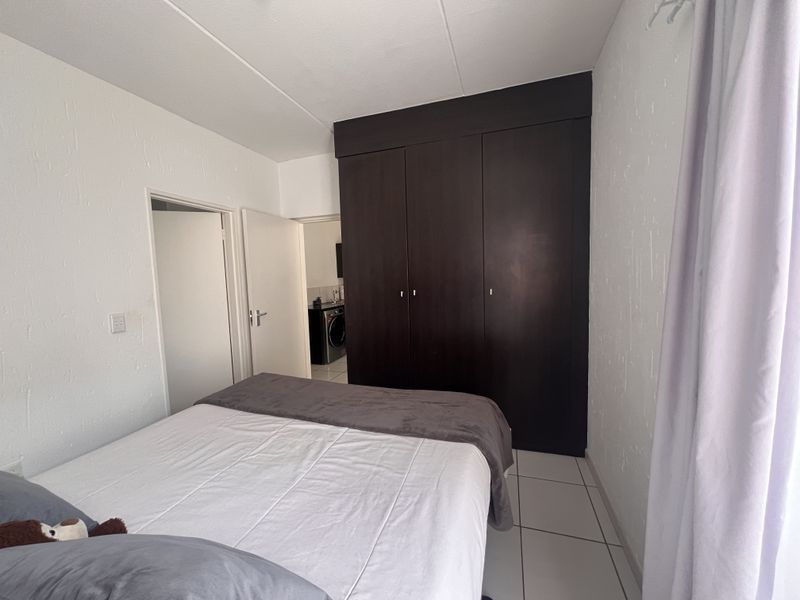 A bedroom featuring dark wood built-in cupboards and neutral tiled flooring, with an adjacent view into a utility area.