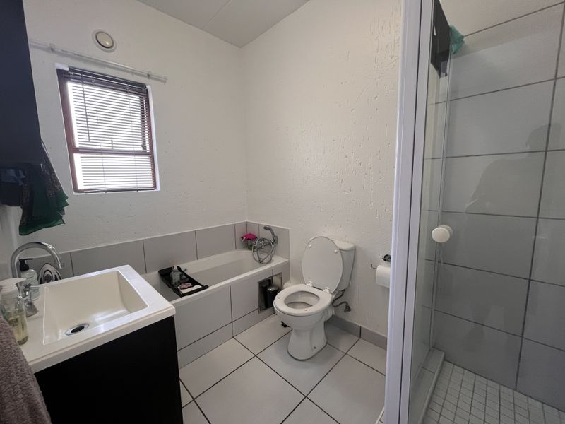 A functional bathroom featuring a built-in bathtub, separate shower enclosure, vanity basin, and toilet with tiled flooring and wall finishes.