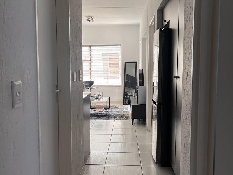 A bright hallway with tiled flooring leading into an open-plan living area, featuring built-in storage cupboards.
