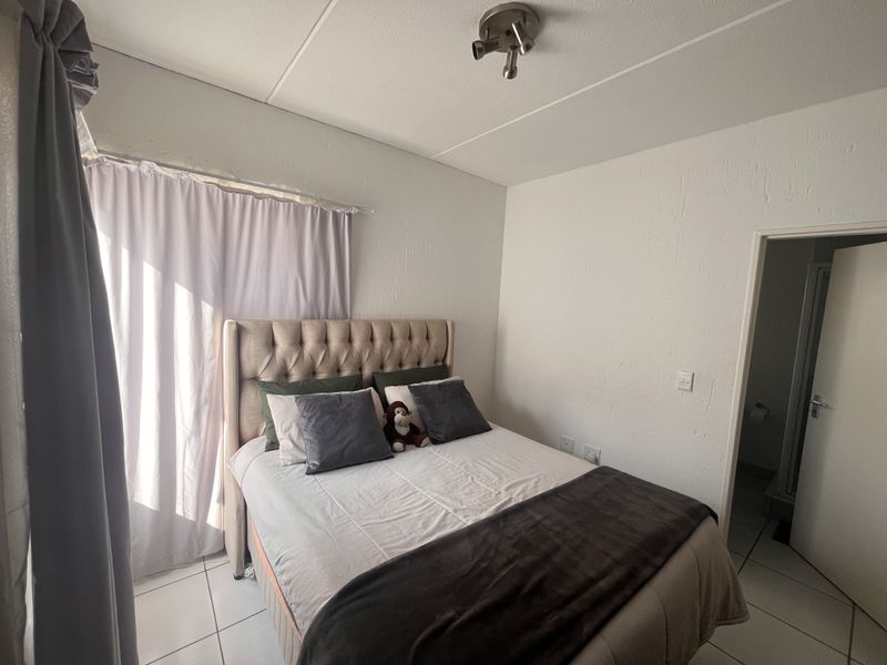 A bedroom featuring tiled flooring, neutral walls, and a ceiling-mounted spotlight fixture, with direct access to an adjoining room.