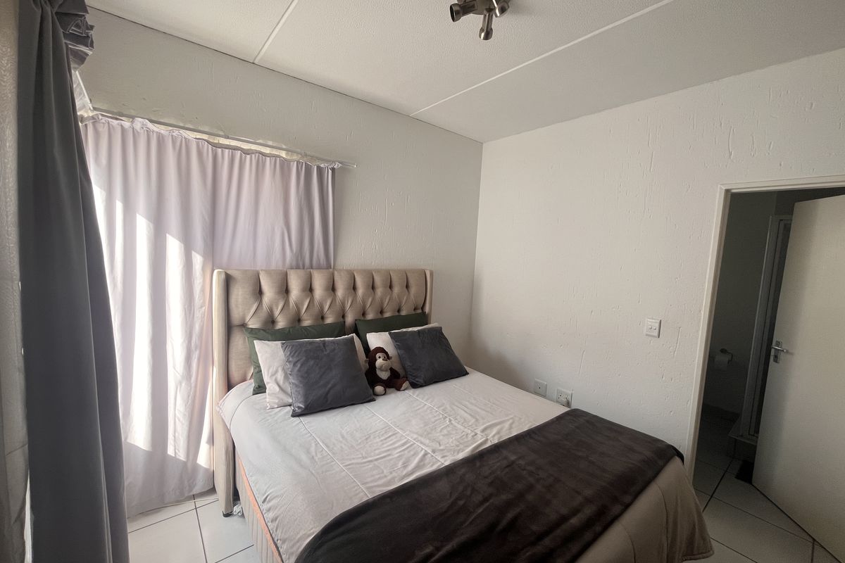 A bedroom featuring tiled flooring, neutral walls, and a ceiling-mounted spotlight fixture, with direct access to an adjoining room.