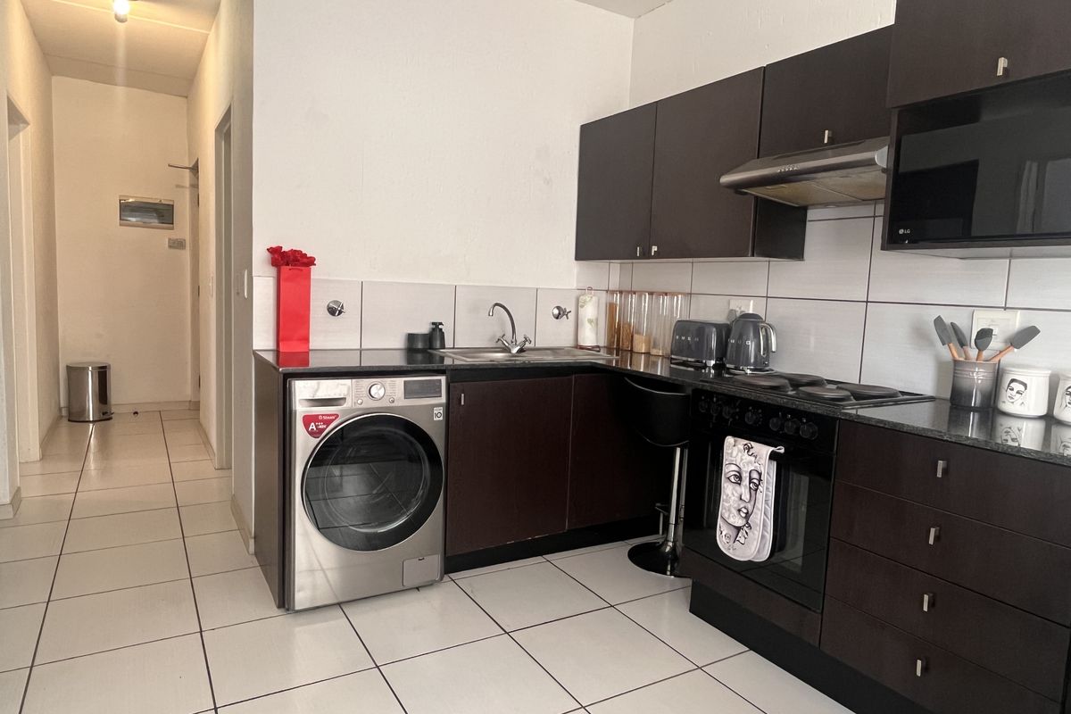 Compact kitchen featuring dark cabinetry, granite countertops, built-in oven, hob, extractor fan, and tiled flooring, with an integrated laundry space.