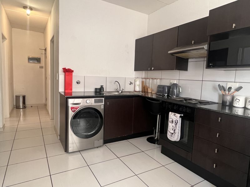 Compact kitchen featuring dark cabinetry, granite countertops, built-in oven, hob, extractor fan, and tiled flooring, with an integrated laundry space.