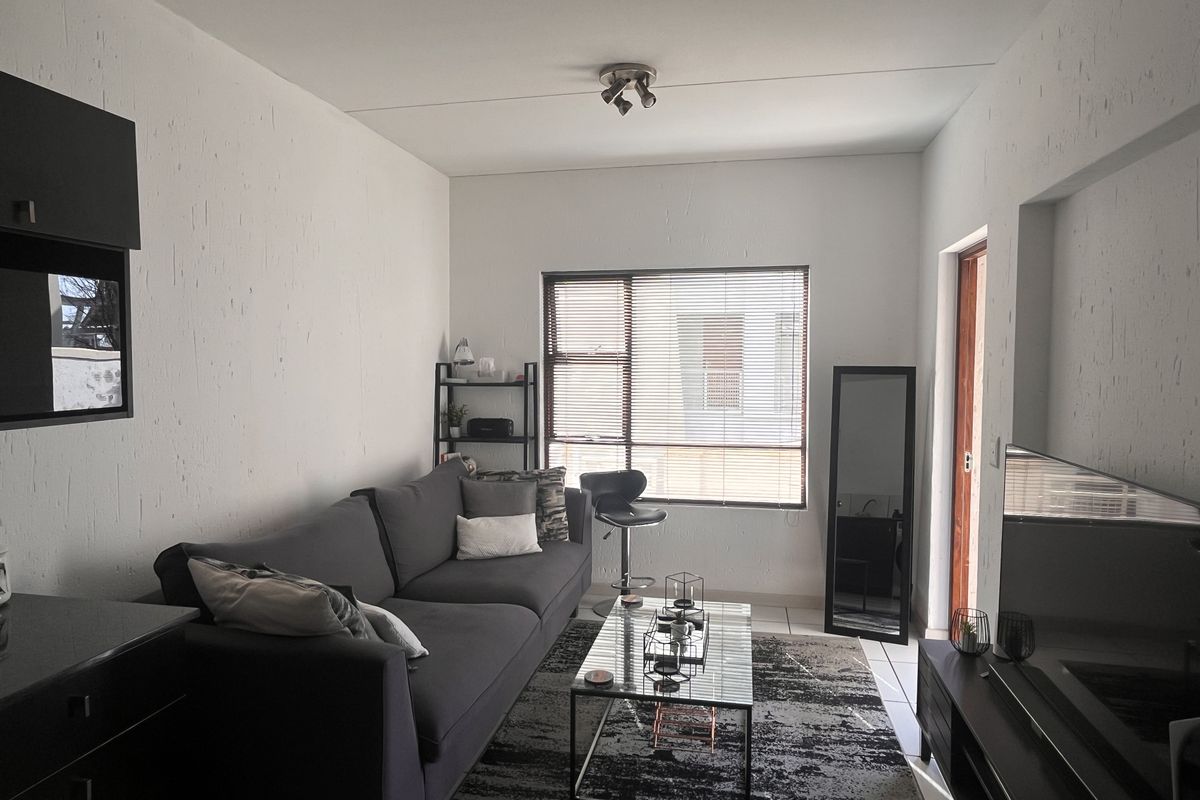 A functional living room featuring tiled flooring, a ceiling-mounted spotlight fixture, and a window fitted with venetian blinds.