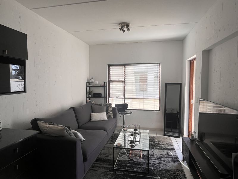 A functional living room featuring tiled flooring, a ceiling-mounted spotlight fixture, and a window fitted with venetian blinds.