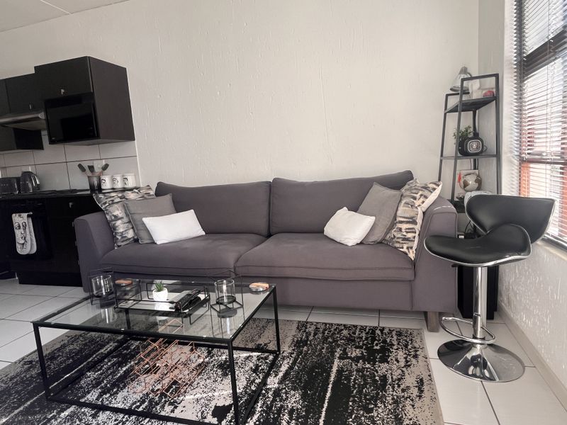An open-plan living area featuring a compact kitchen with black cabinetry and tiled flooring, seamlessly integrated with a comfortable lounge space.