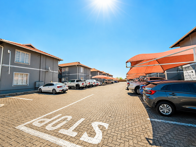Exterior view of the apartment complex featuring paved parking areas, shade cloth carports, and well-maintained building facades.