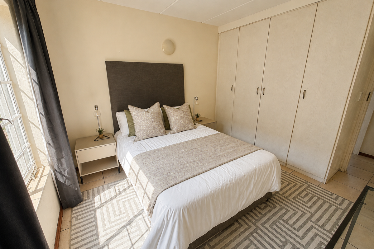 A well-lit bedroom featuring built-in cupboards, tiled flooring, and a window with security bars, offering a functional and comfortable living space.
