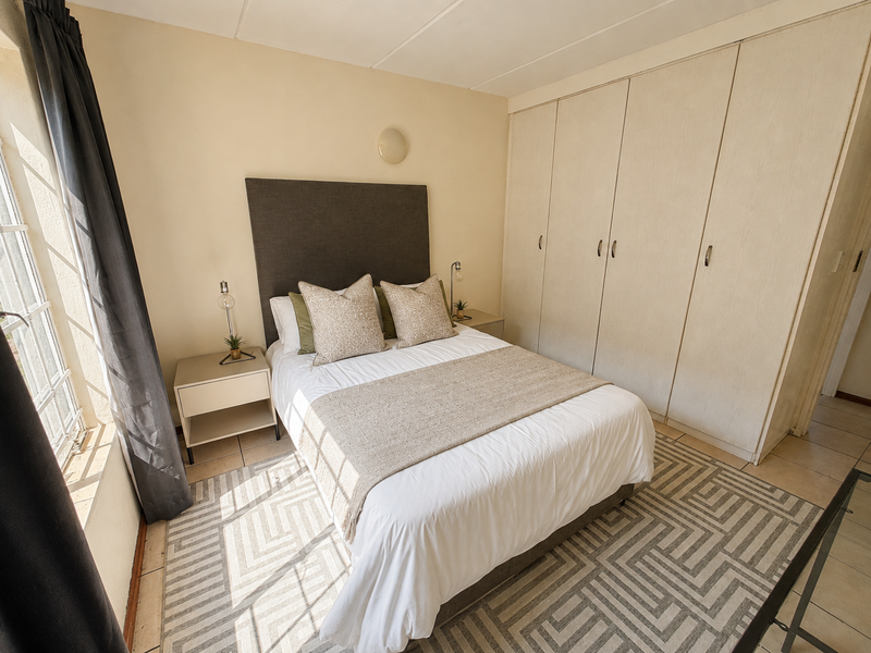 A well-lit bedroom featuring built-in cupboards, tiled flooring, and a window with security bars, offering a functional and comfortable living space.