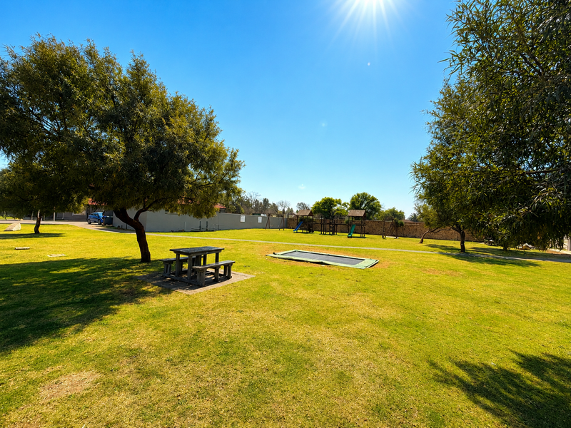 A spacious, well-maintained communal garden area featuring mature trees, expansive lawn, and perimeter walling.