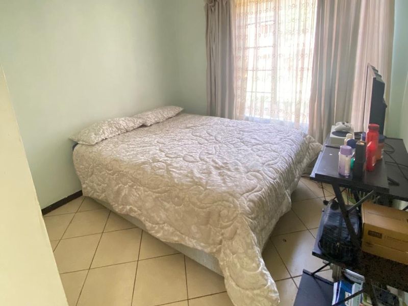 A functional bedroom featuring tiled flooring and natural light through a window with installed curtain rails.