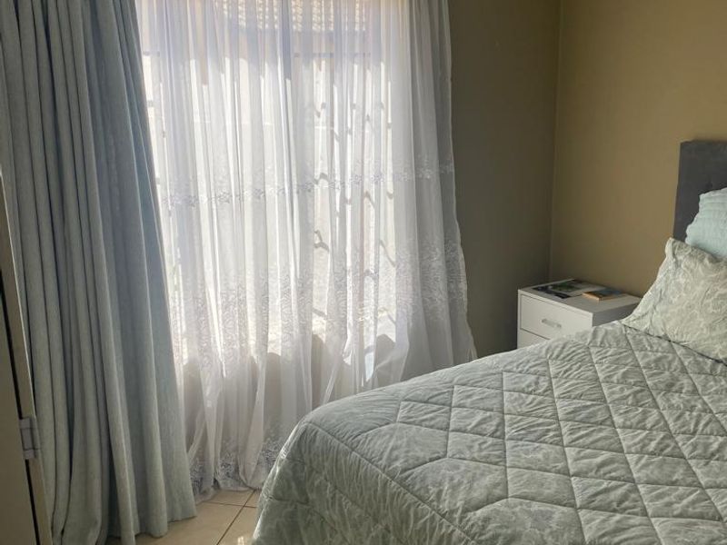 A bedroom featuring tiled flooring and a sliding glass door with curtains, providing natural light.