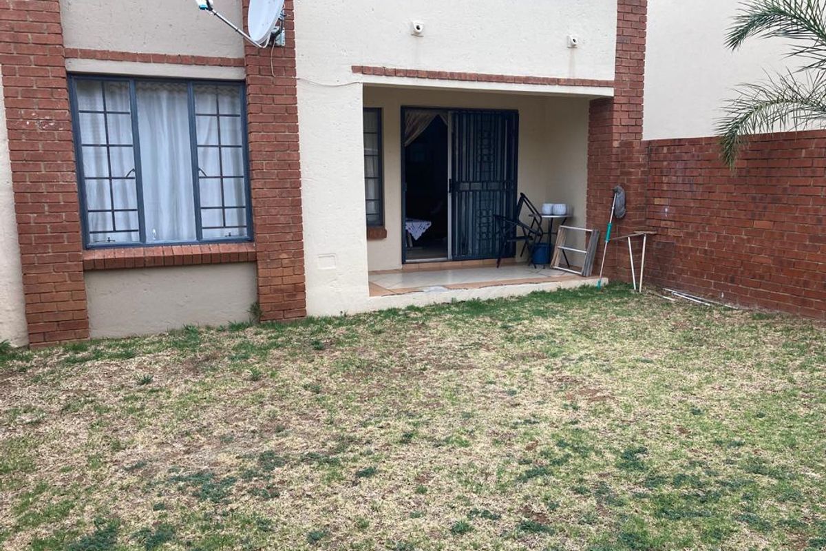 Rear view of the apartment featuring a small tiled patio, brick facade, and a private garden area.