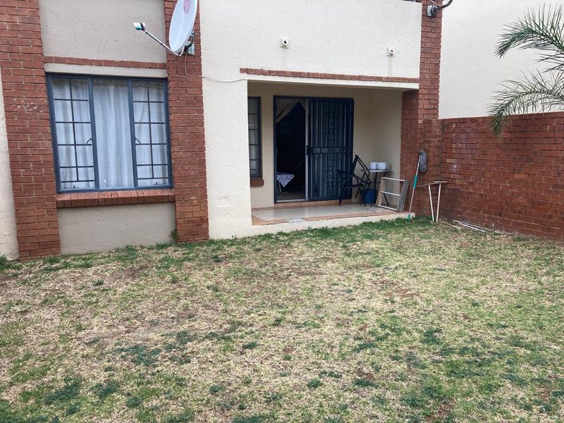 Rear view of the apartment featuring a small tiled patio, brick facade, and a private garden area.