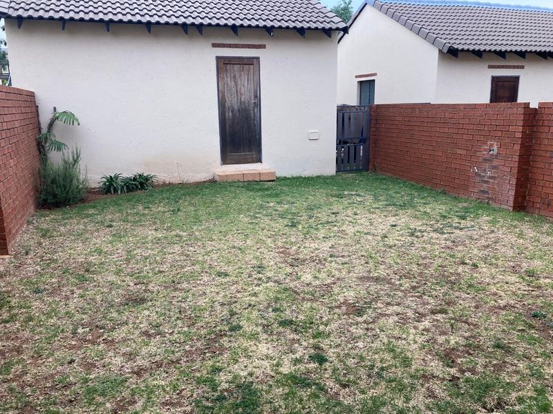 A private rear garden area featuring a lawn, enclosed by brick boundary walls, with access to the main building structure via a wooden door.