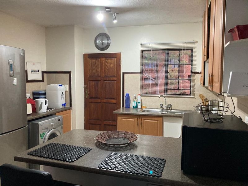 A functional kitchen featuring wooden cabinetry, laminate countertops, a stainless steel sink, and a tiled backsplash with a window providing natural light.